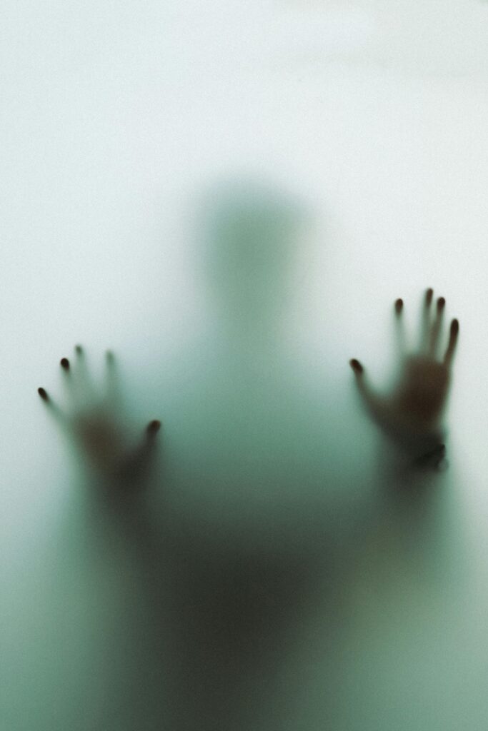 Eerie silhouette of a person behind frosted glass with hands pressed against the surface.